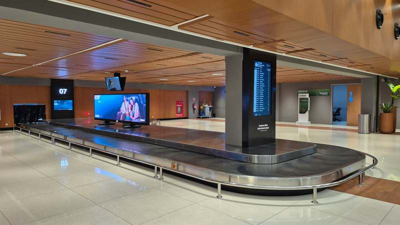 Traveler at airport luggage carousel with one suitcase, looking concerned while others collect bags